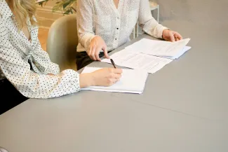 woman signing on white printer paper beside woman about to touch the documents by Gabrielle Henderson courtesy of Unsplash.